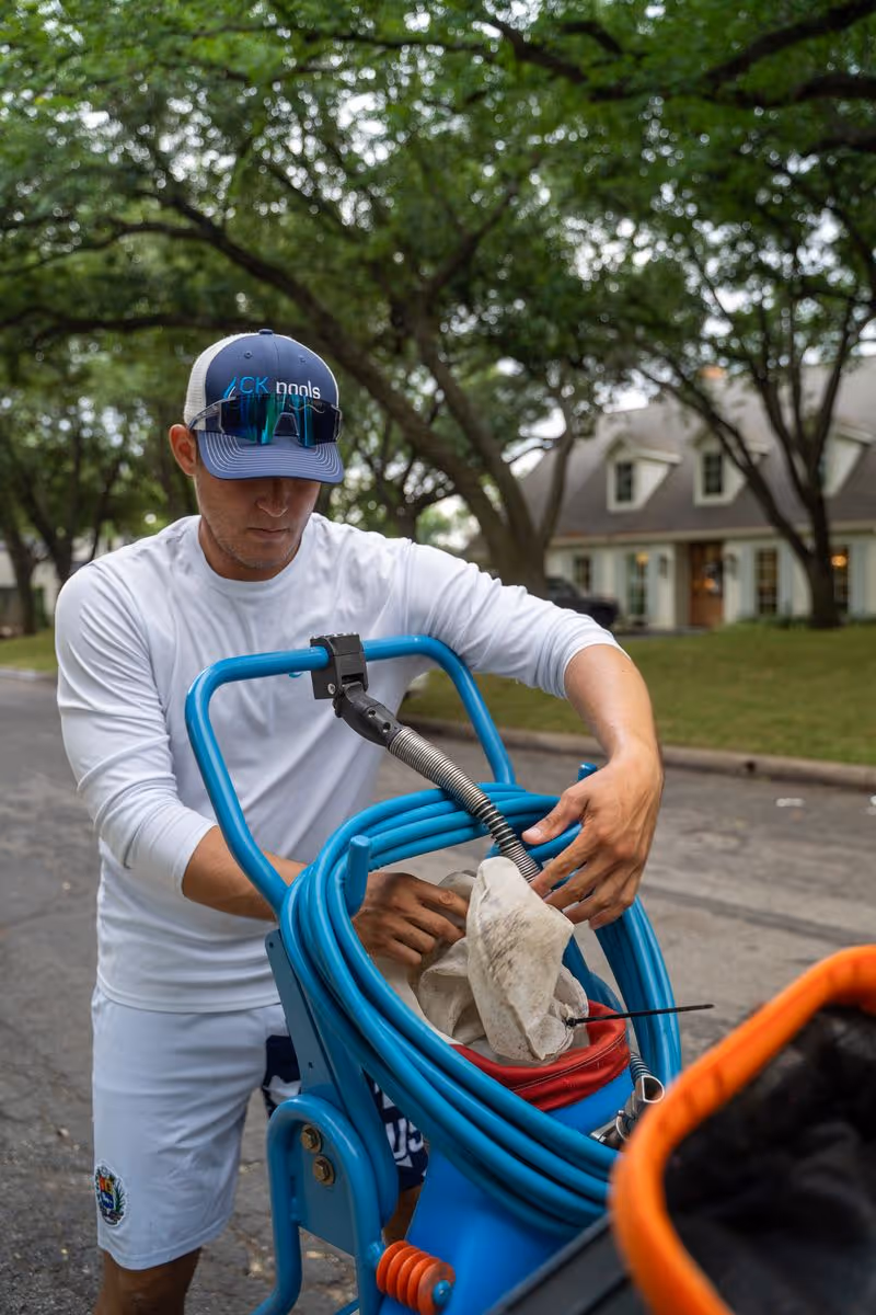 Pool service technician preparing equipment beside a residential property