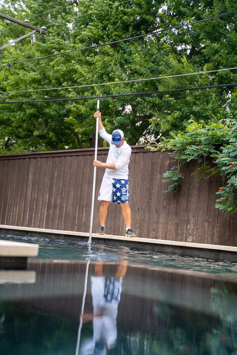 CK Pools technician brushing a residential swimming pool with a telescopic pole