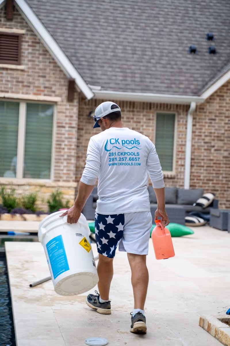 CK Pools technician carrying pool maintenance chemicals beside a residential pool