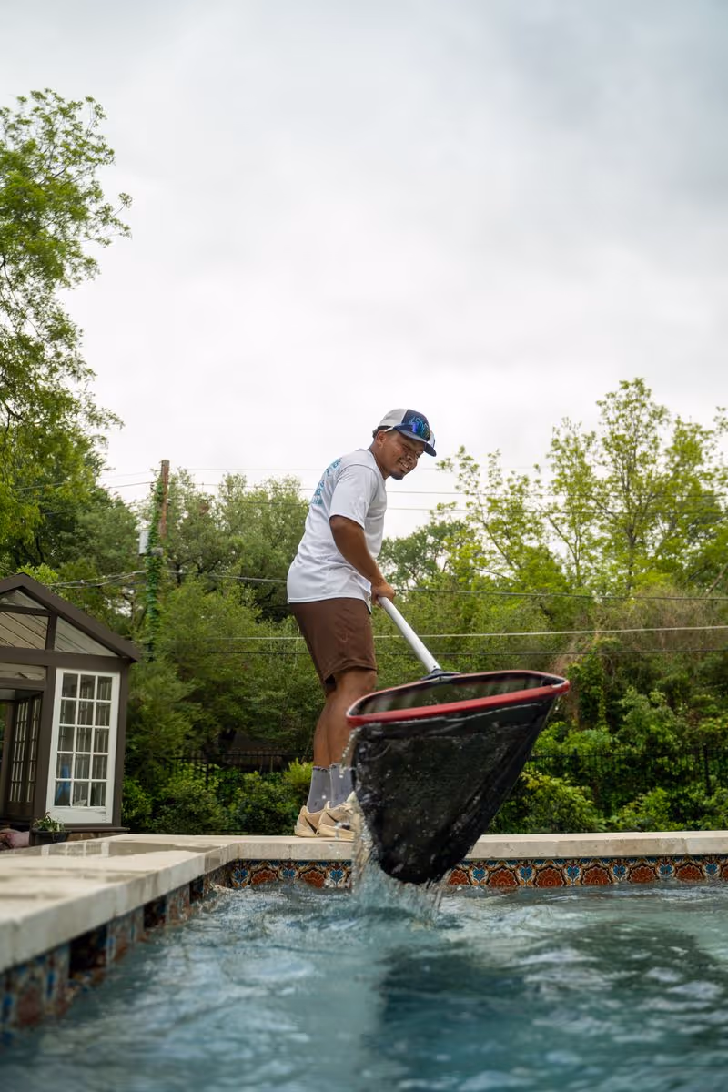 Pool technician removing debris with a skimmer net during residential pool maintenance