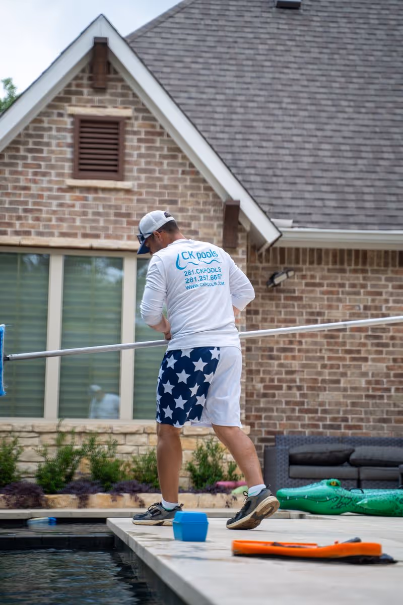 Pool technician cleaning a backyard pool beside a brick home