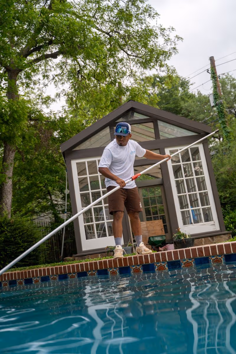 CK Pools technician cleaning a backyard swimming pool with a telescopic pole