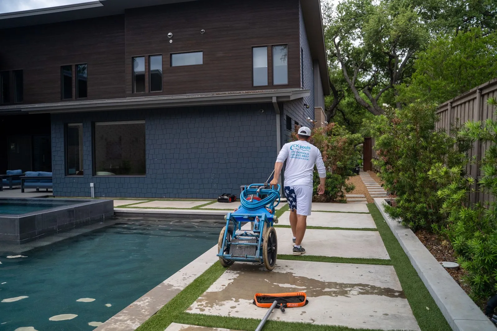 CK Pools technician transporting maintenance equipment beside a modern residential pool