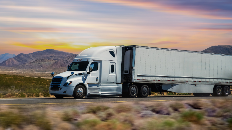 White semi truck pulling a dry van trailer on a desert highway at sunset