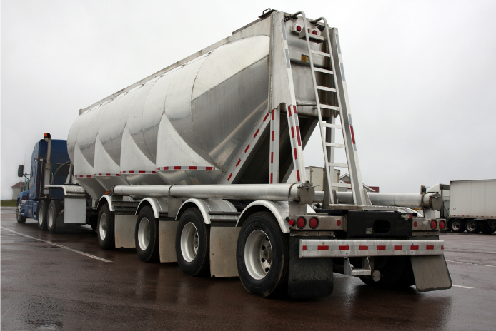 Silver pneumatic dry bulk trailer parked on wet pavement