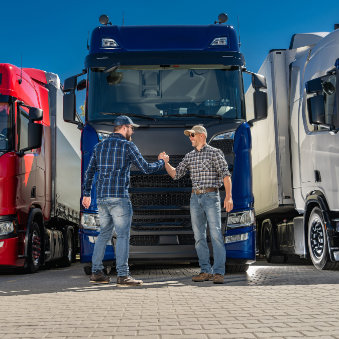 Two truck drivers shaking hands in front of their semi trucks