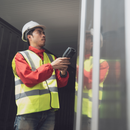 Warehouse worker in a hard hat and safety vest using a handheld scanner at a trailer