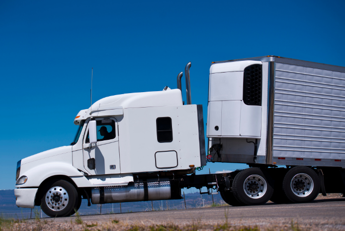 White semi truck with a refrigerated trailer under a blue sky
