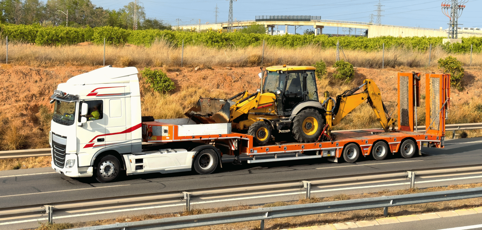Backhoe loader hauled on a lowboy trailer along a highway