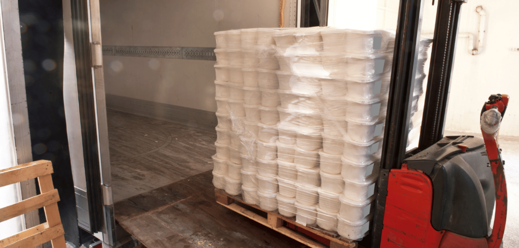 Pallet of packaged goods being loaded into a refrigerated trailer with a pallet jack