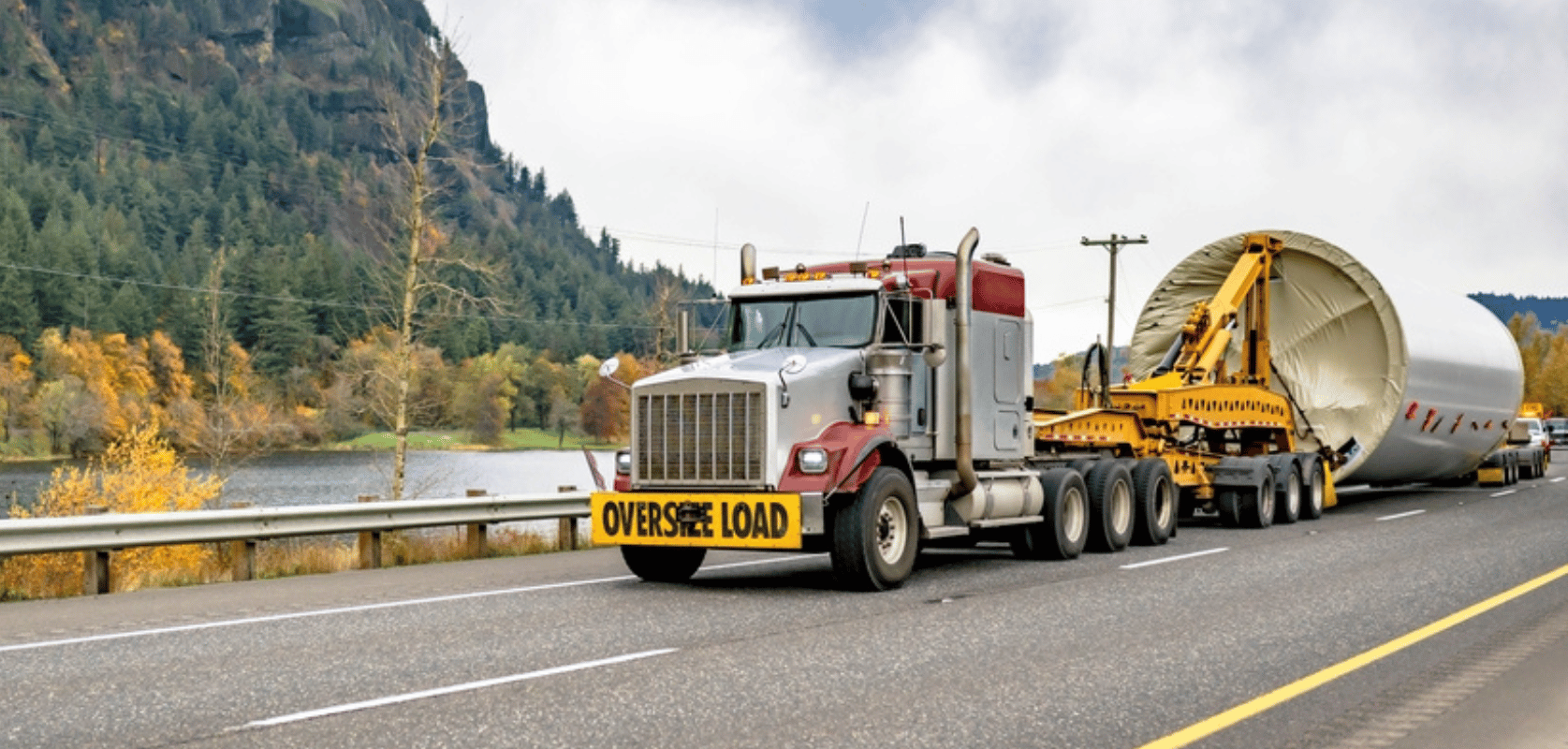 Semi truck with an Oversize Load banner hauling a large industrial component on a mountain highway