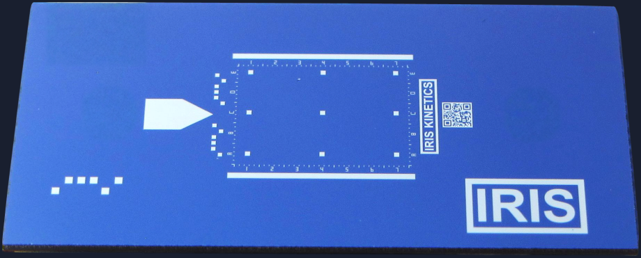 The IRIS chip, photographed from above: a blue 8 by 16 mm silicon chip with an alignment arrow, a scale grid, a QR code and the IRIS mark