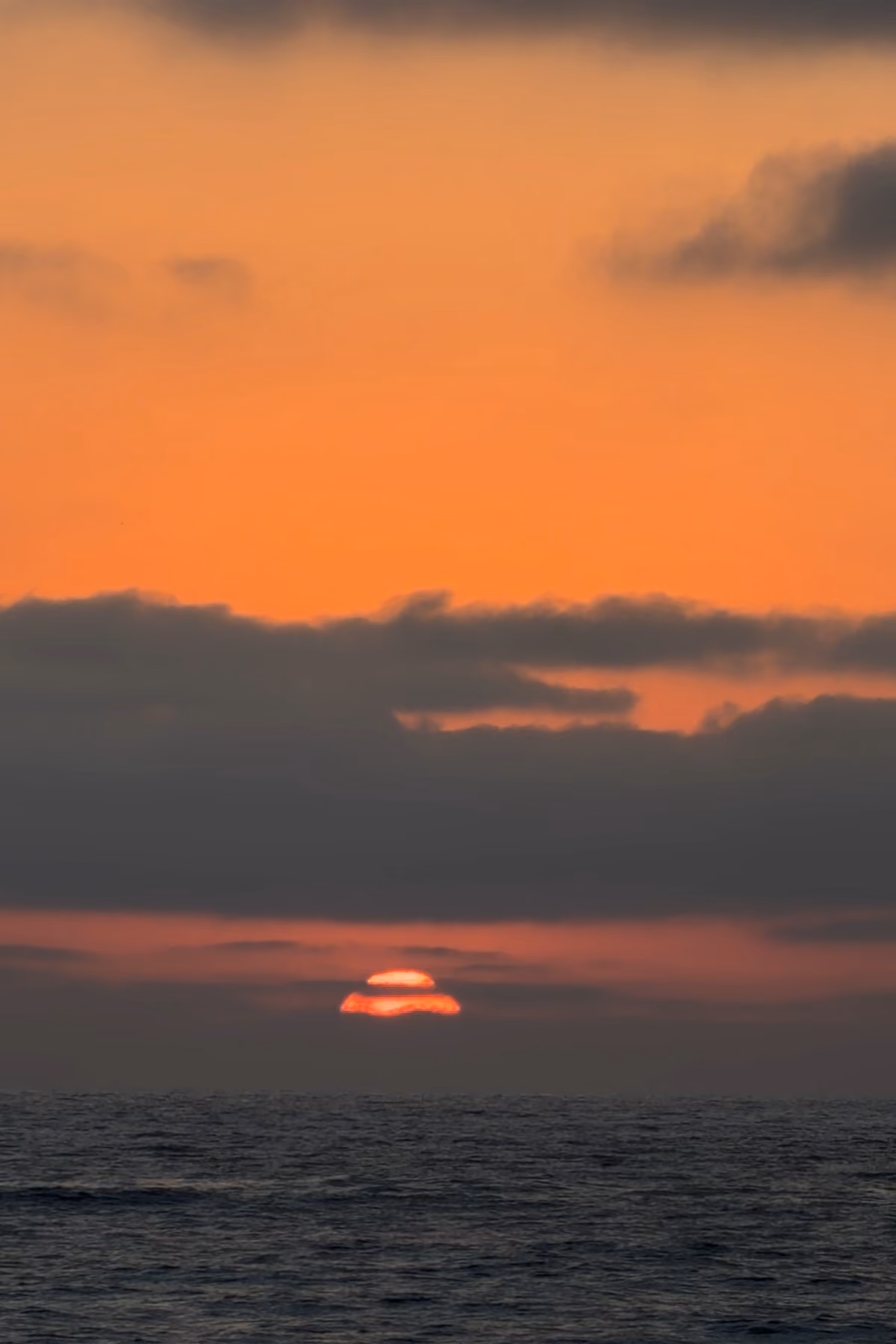 Sun setting over the Pacific Ocean beneath orange clouds