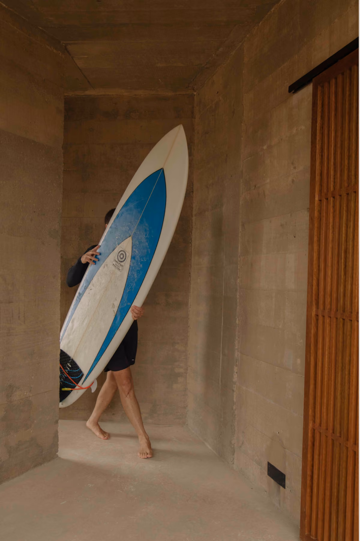 Guest carrying a surfboard through a concrete corridor