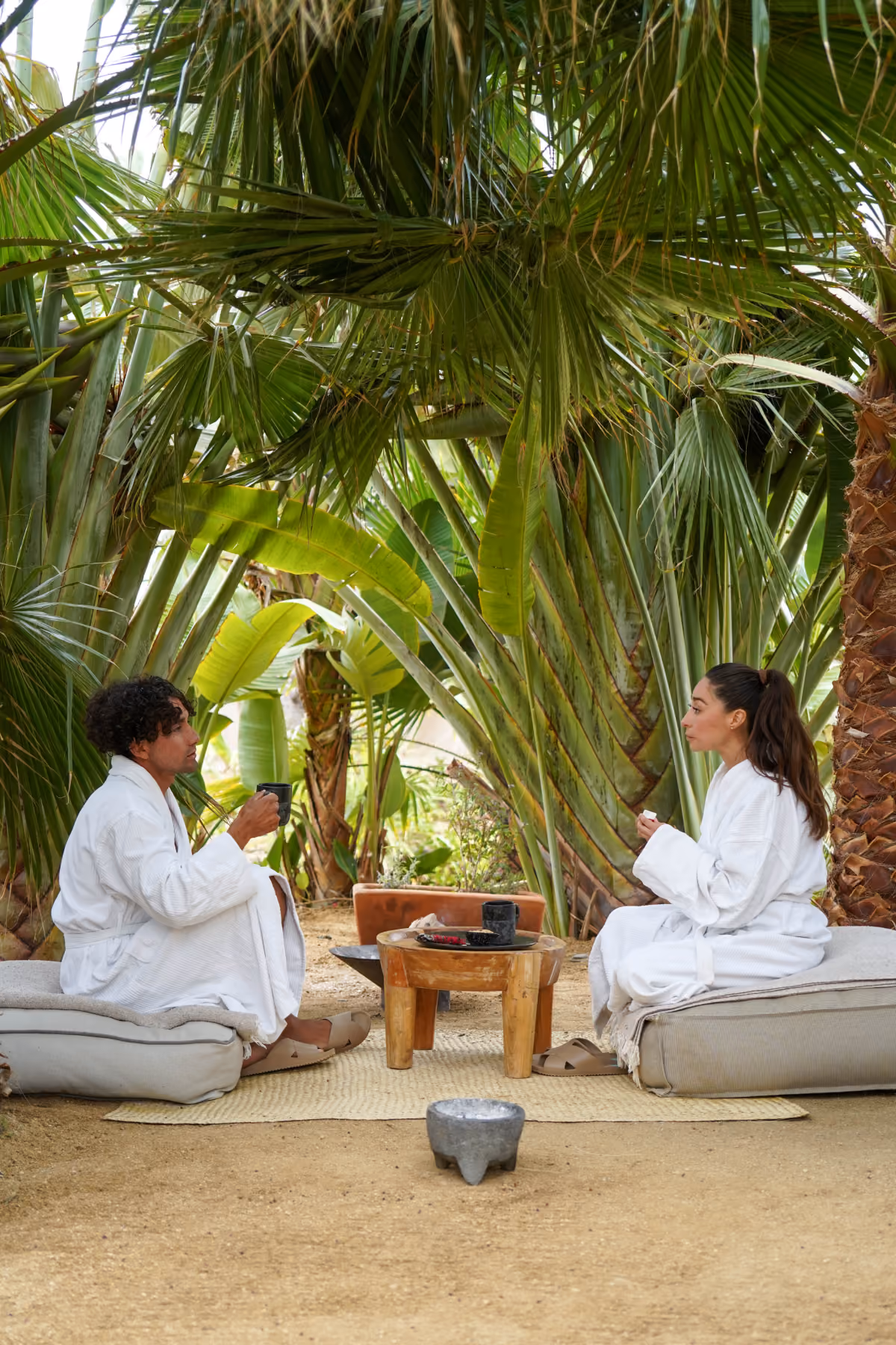 Two guests in white robes during a garden ritual among palms