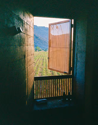 Window in a rammed-earth wall opening onto green farm fields