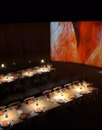 Long dinner tables in a dark room with projected art