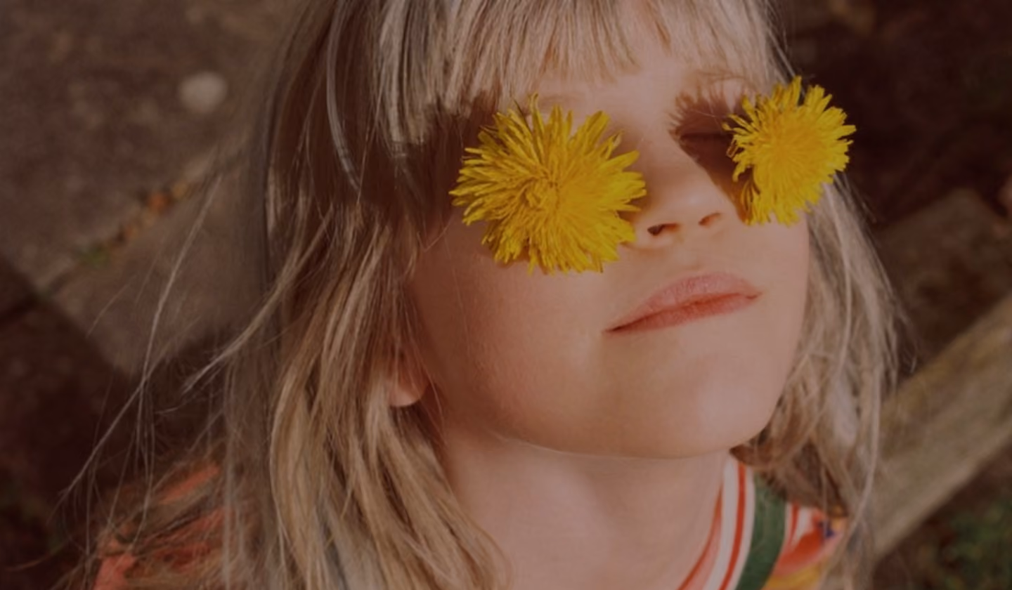 Smiling child with yellow flowers over her eyes