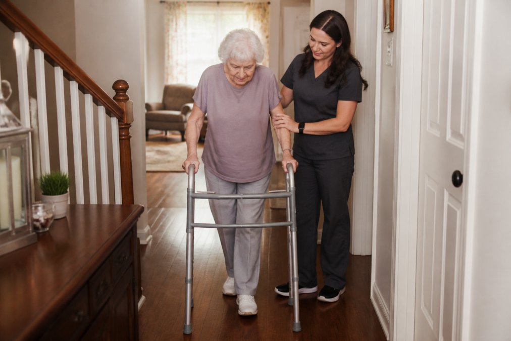 Older adult using a walker while moving through their home with a caregiver nearby providing support and stability