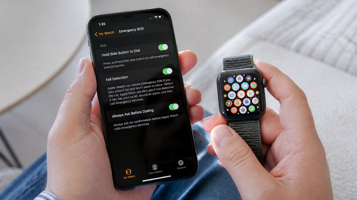 Close-up of hands holding an iPhone and Apple Watch together, showing the Watch app interface on the iPhone screen with fall detection settings visible