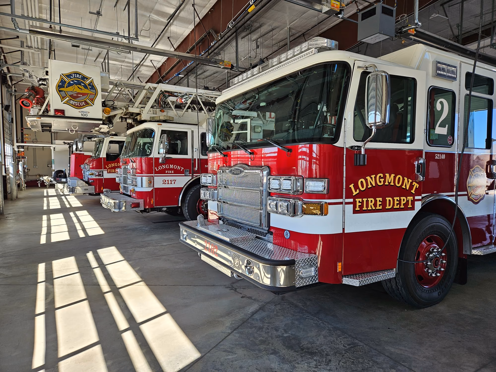 Longmont Fire Department engines parked in the station bay, sunlight across the floor