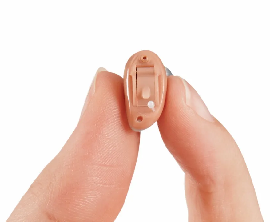Hautfarbenes Mini-Hörgerät zwischen zwei Fingerspitzen