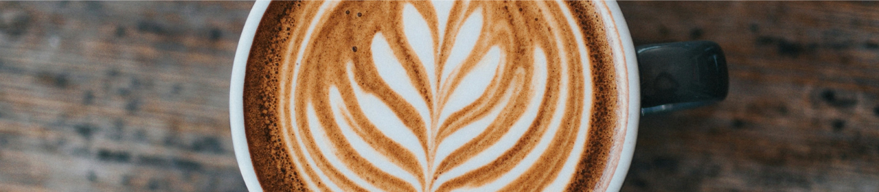Tasse de café latte avec un art en mousse représentant une feuille symétrique sur une surface en bois.