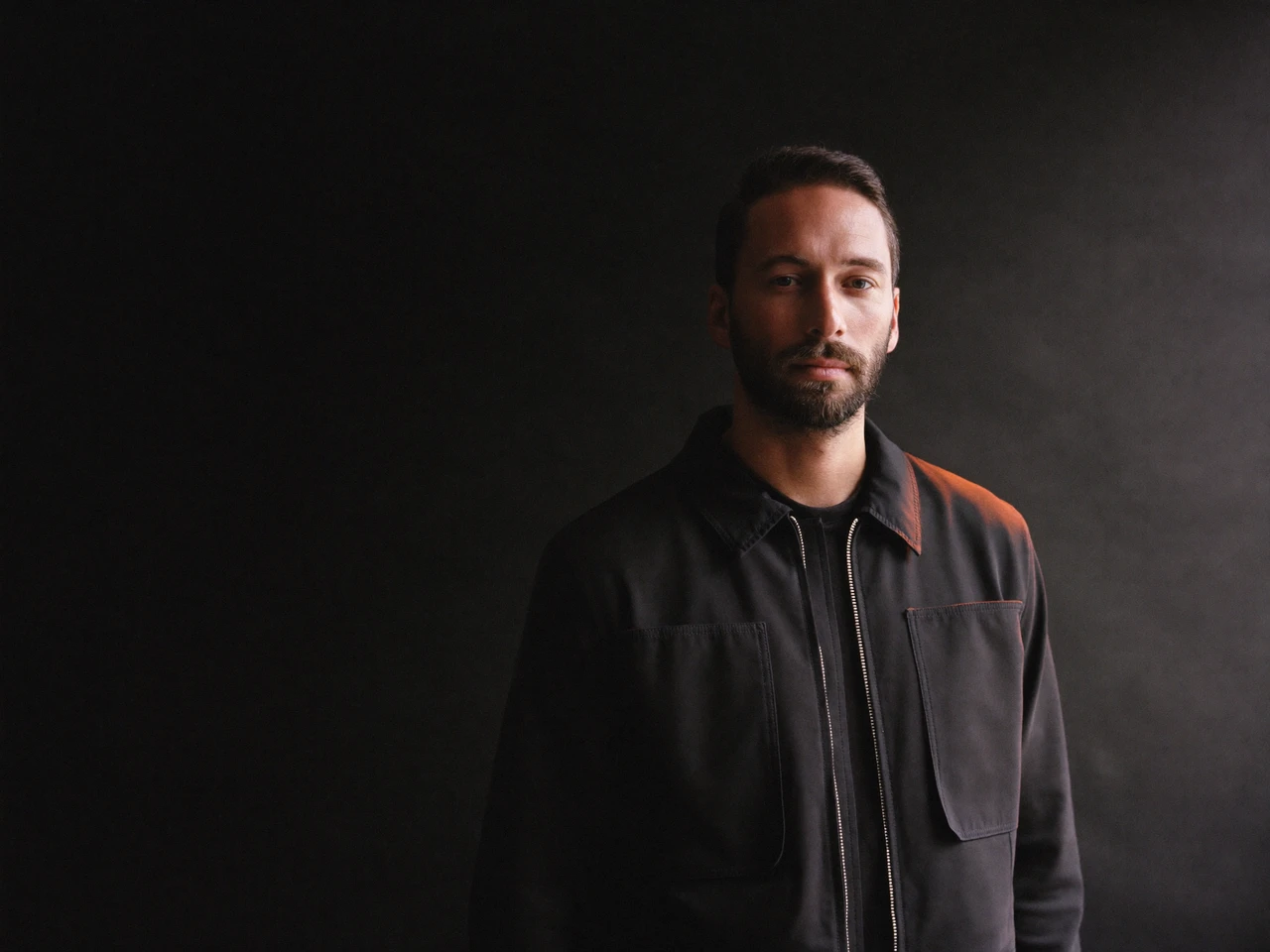 Portrait of a designer in a dark jacket against a dark studio backdrop