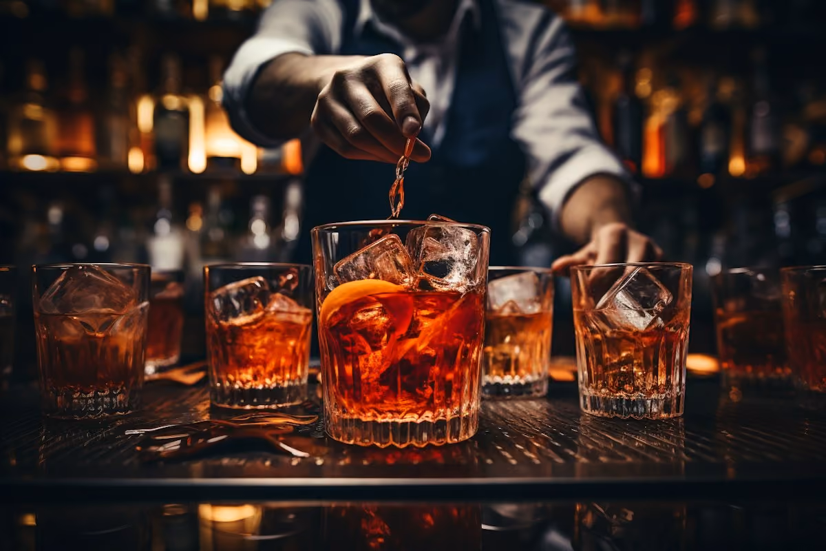Bartender pouring over ice into rows of old fashioned glasses