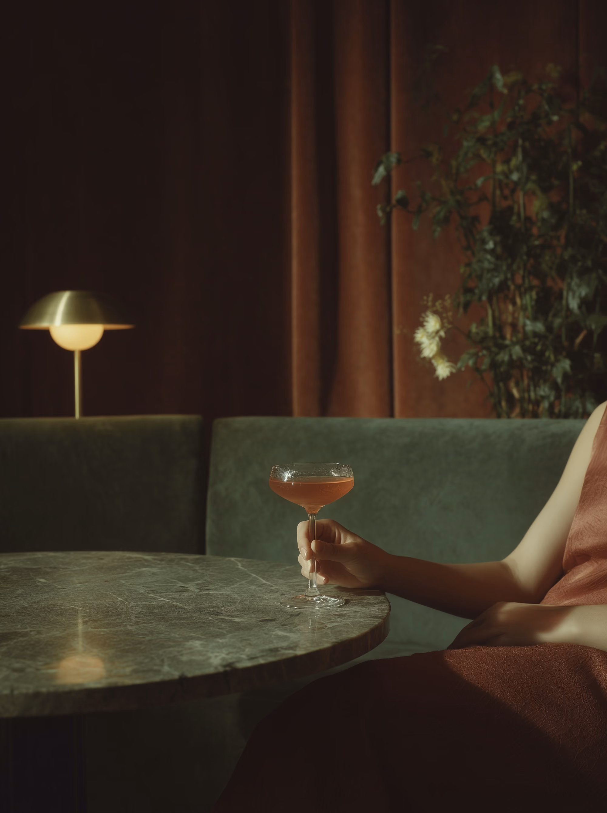 Hand holding a coupe cocktail beside a green velvet banquette