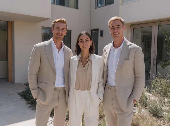 Three people wearing beige suits and smiling, standing outside a modern building.