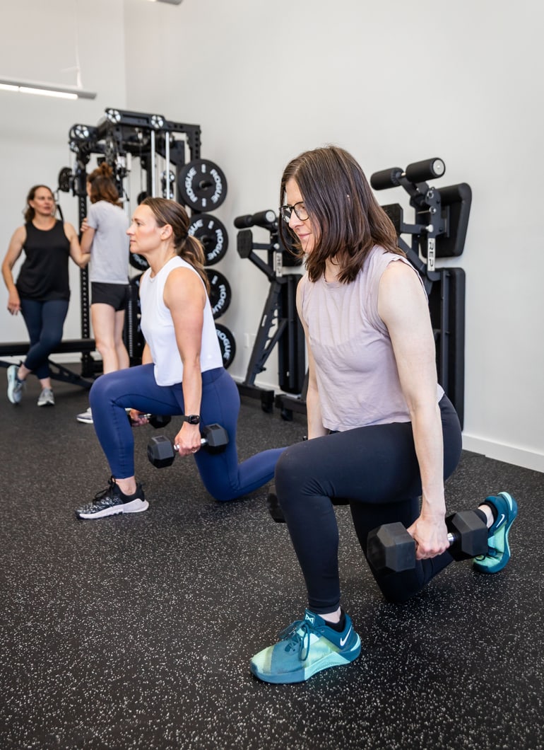 Two women doing dumbbell lunges in a strength class