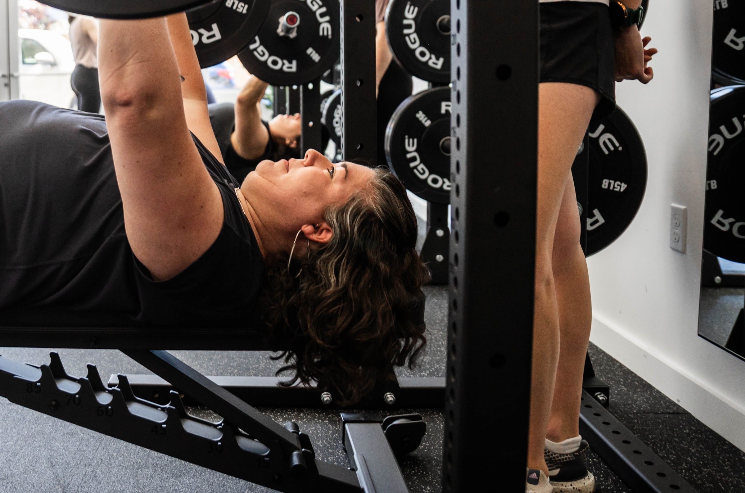 A member bench pressing in front of a rack at Women's Strength Collective in Portland, OR