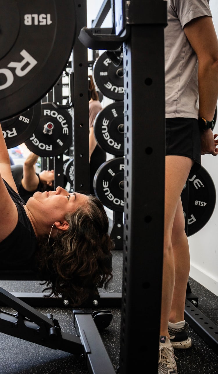 A member bench pressing in front of a rack at Women's Strength Collective in Portland, OR