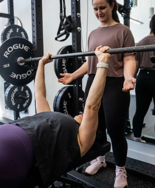 Coach spotting a member on the bench press at Women's Strength Collective in Portland, OR