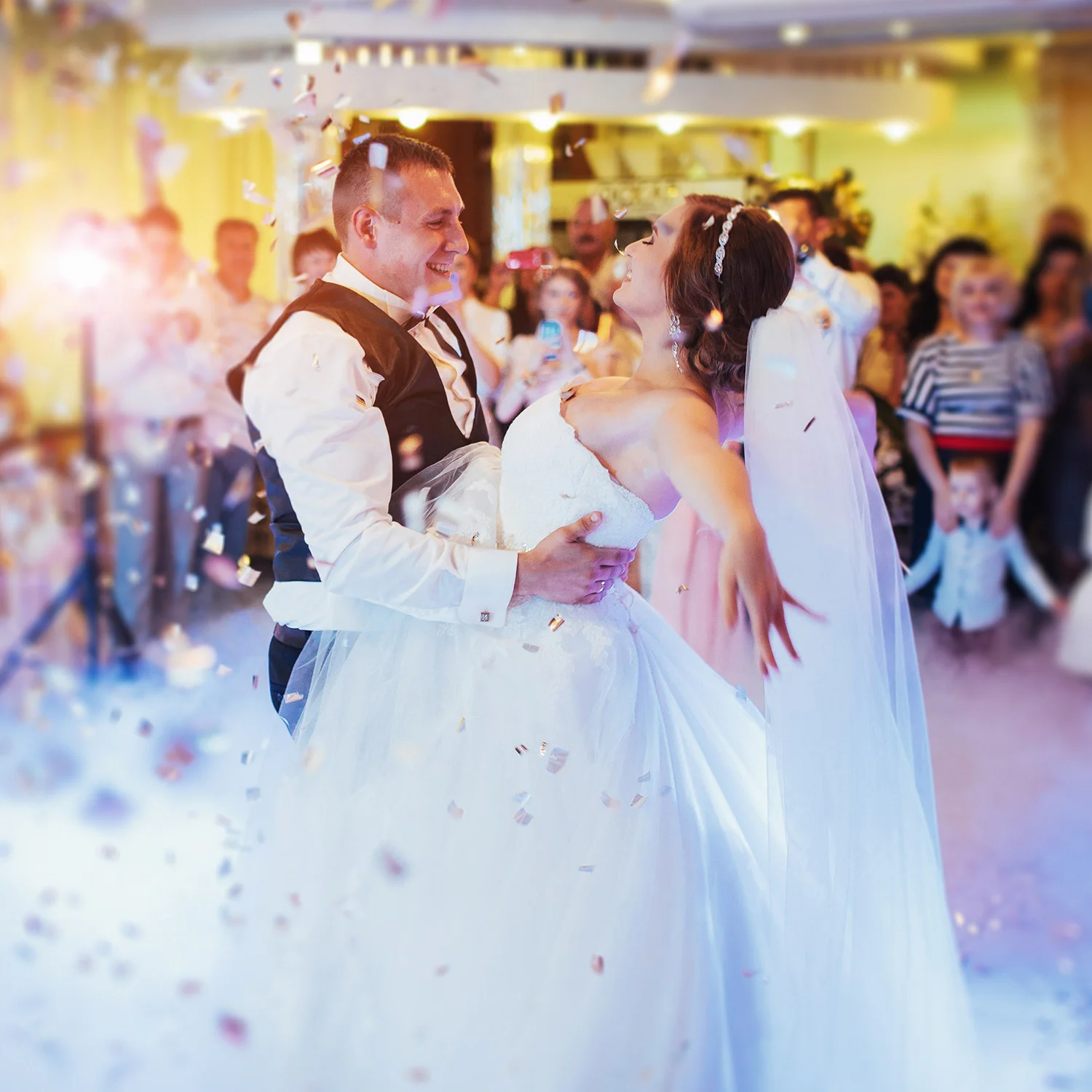 Bride and groom sharing their first dance surrounded by confetti at a wedding reception, with guests celebrating in the background.