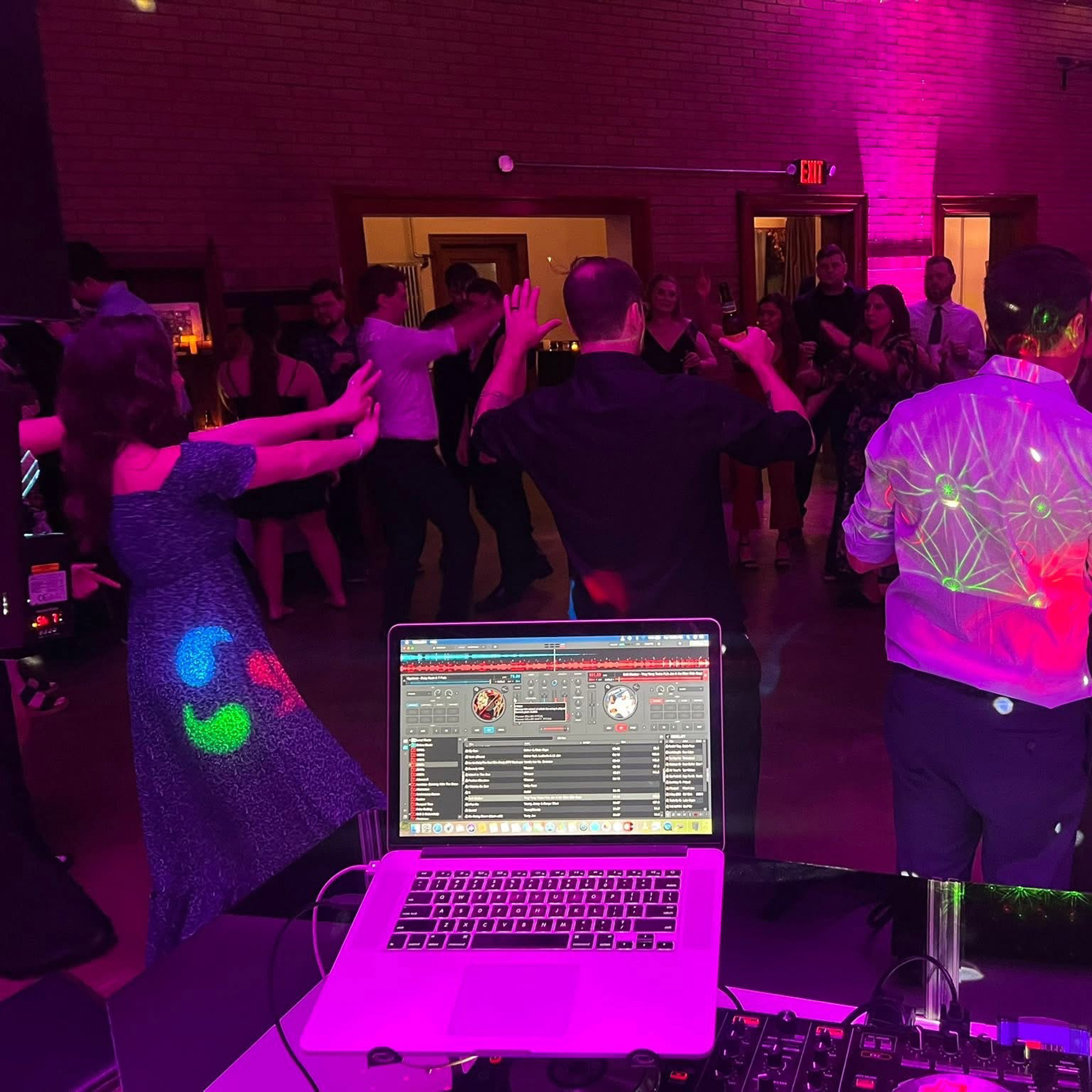View from the DJ booth of guests dancing under purple lighting at a wedding reception, with Serato software visible on the laptop screen.