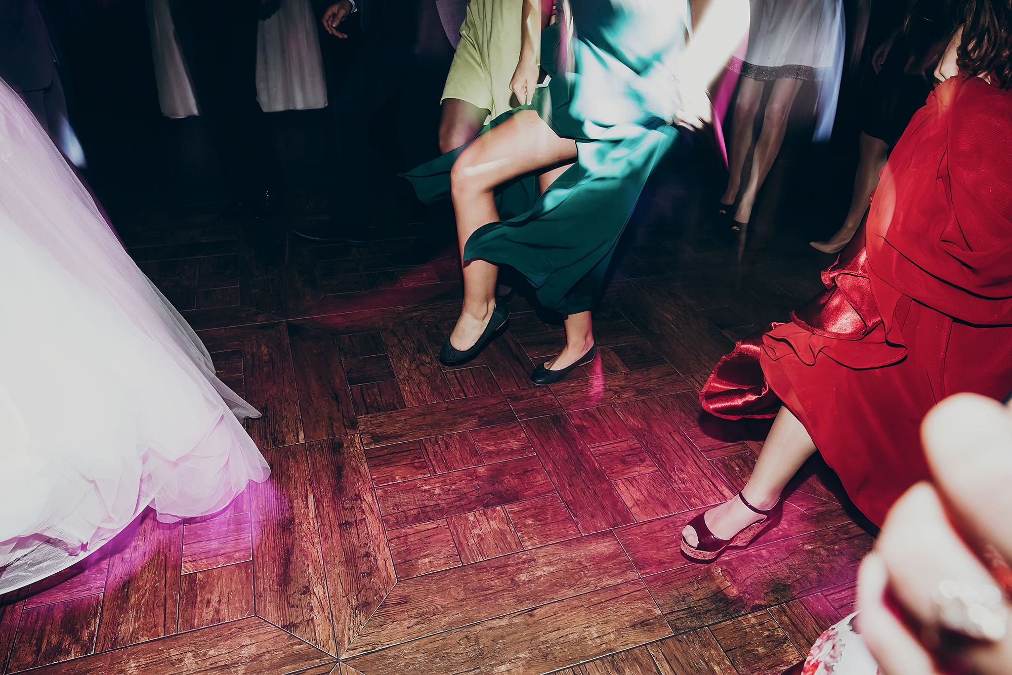 Wedding guests dancing on a dance floor lit with colorful uplighting, dresses in motion