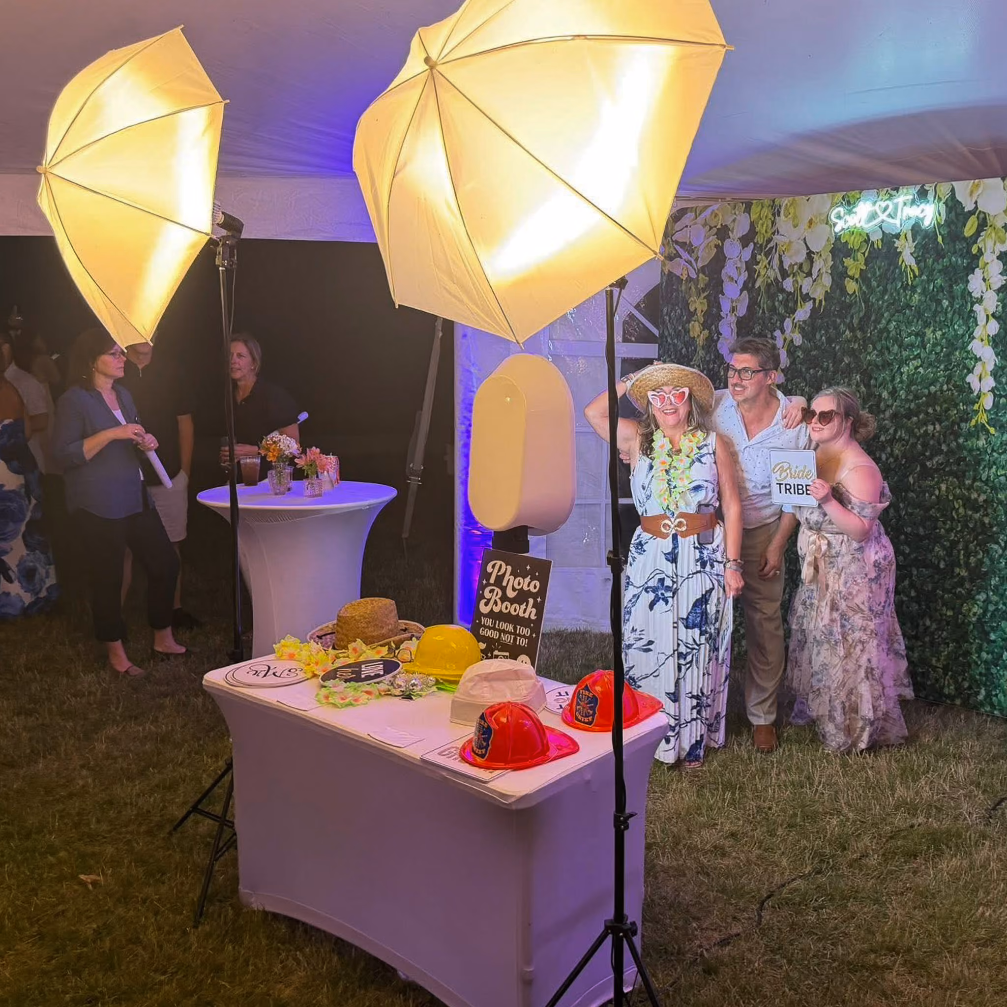 Group of women and a young girl laughing together in a photo booth at a wedding, set against a floral curtain backdrop