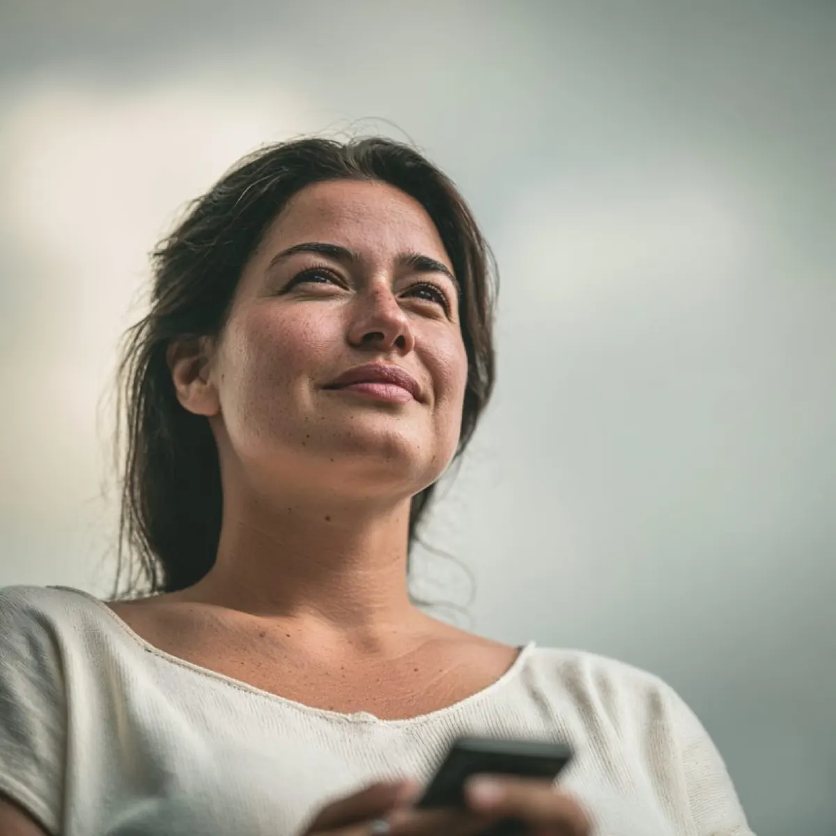Frau mit dem Handy in der Hand, die aufschaut und lächelt