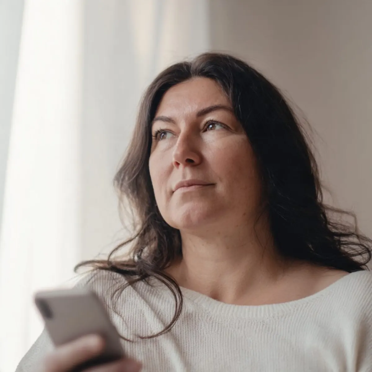 Frau mit dem Handy in der Hand am Fenster