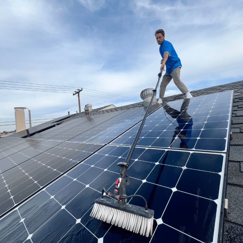 Technician cleaning rooftop solar panels with a water-fed brush