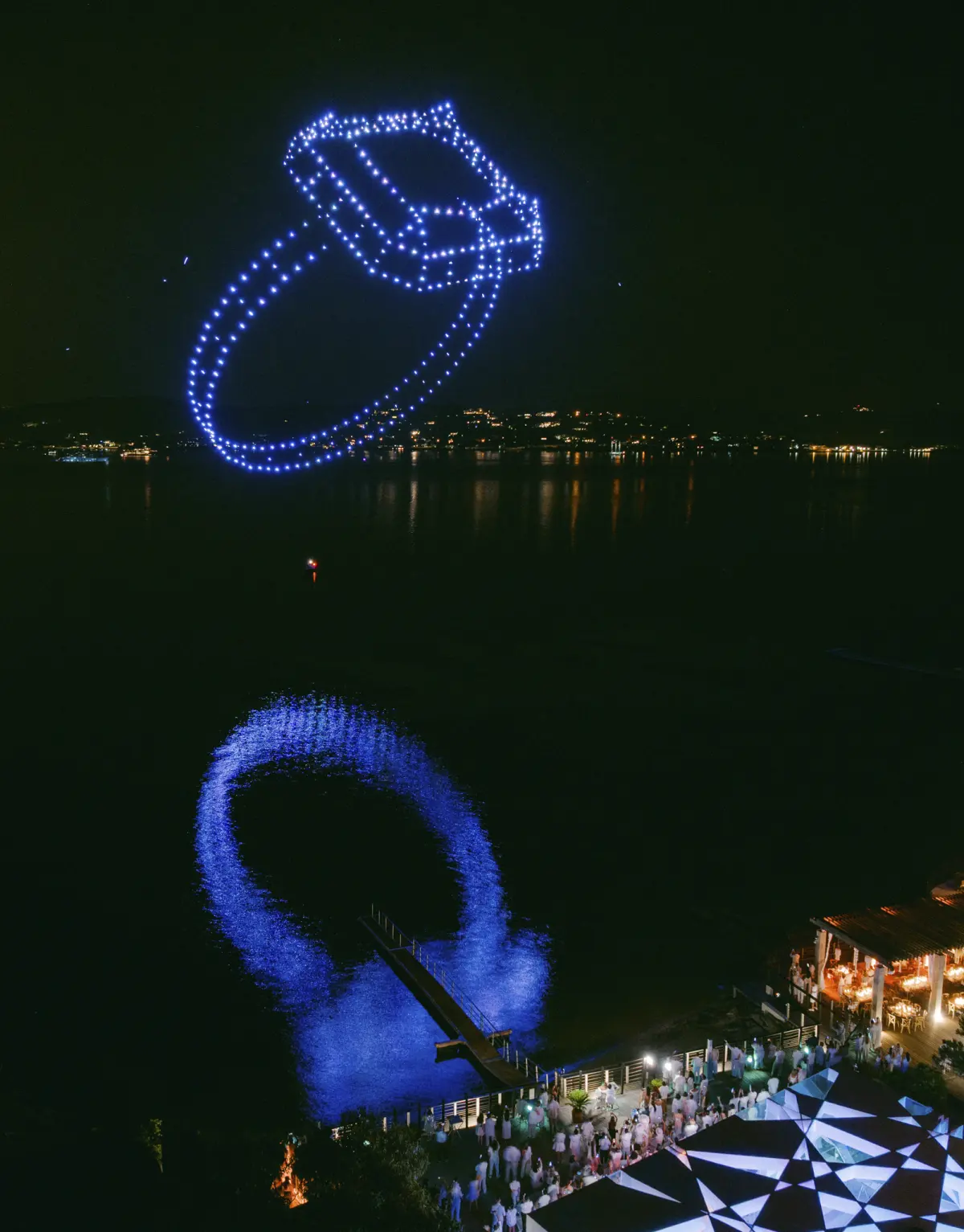 Une bague de fiançailles lumineuse dessinée par les drones au-dessus d’un lac, devant les invités d’un mariage
