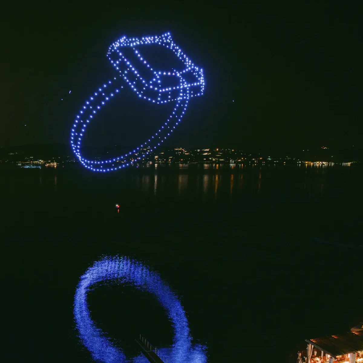 Une bague de fiançailles lumineuse dessinée par les drones au-dessus d’un lac, devant les invités d’un mariage