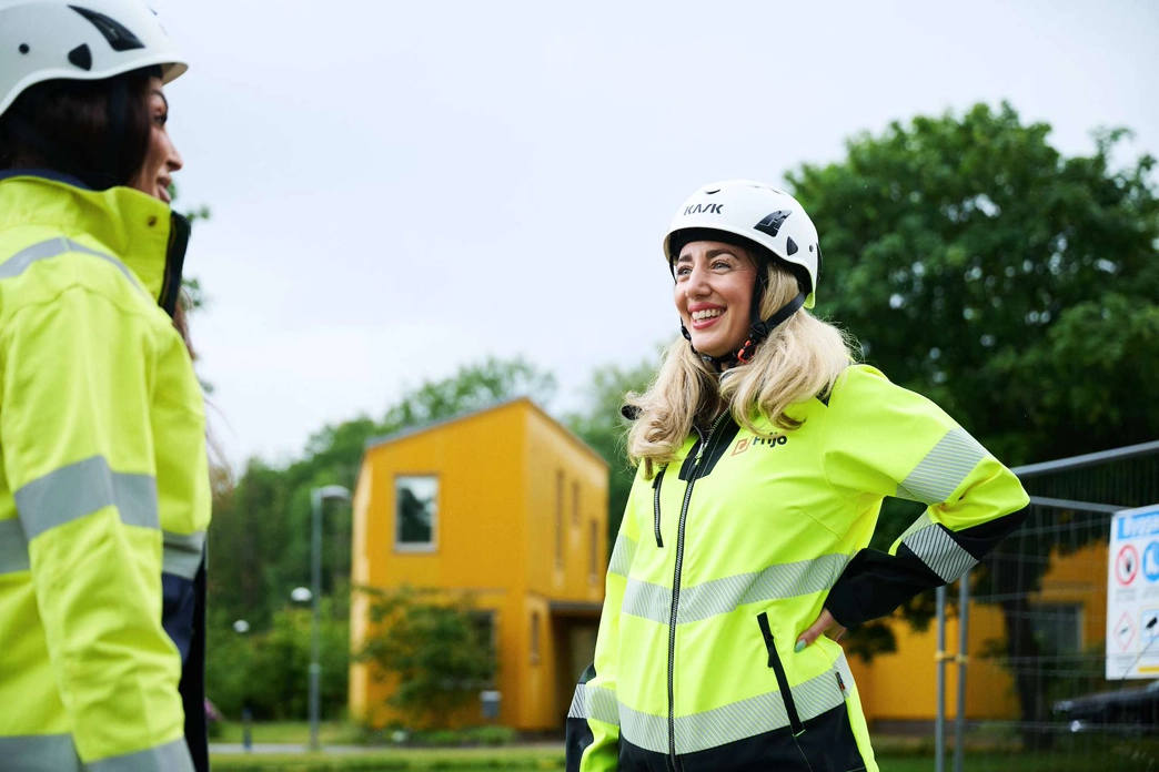 Två medarbetare som står och ler mot varandra i varselkläder ute i tjänst.