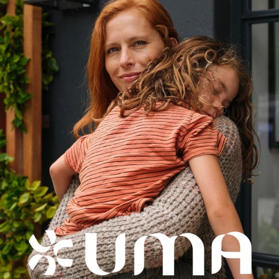 Uma : une femme qui porte dans ses bras un enfant endormi, devant une maison, avec le logo en blanc