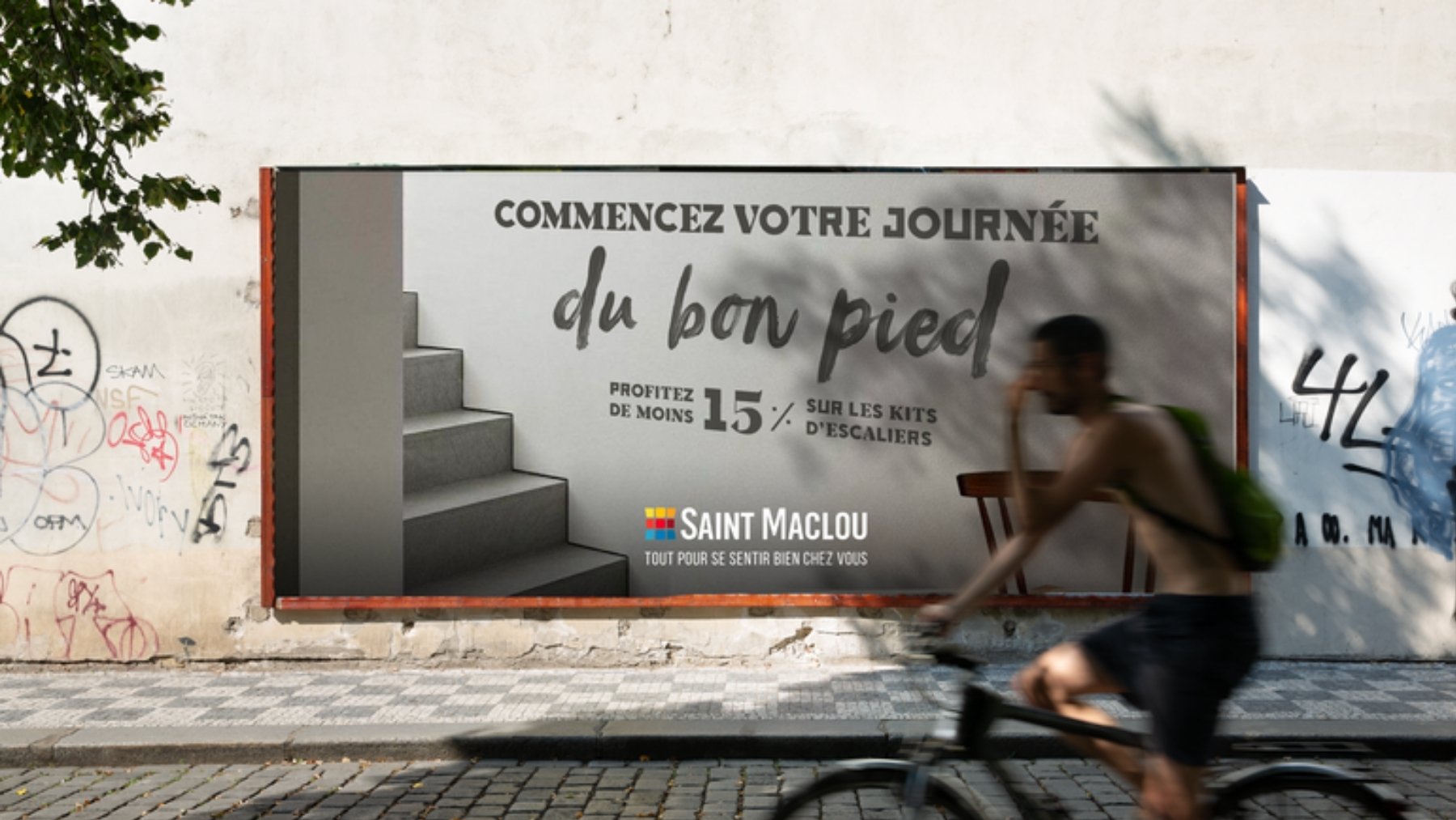 Saint Maclou : l’affiche « Commencez votre journée du bon pied » sur un mur tagué, un escalier et une chaise, signée « Tout pour se sentir bien chez vous », un cycliste au premier plan