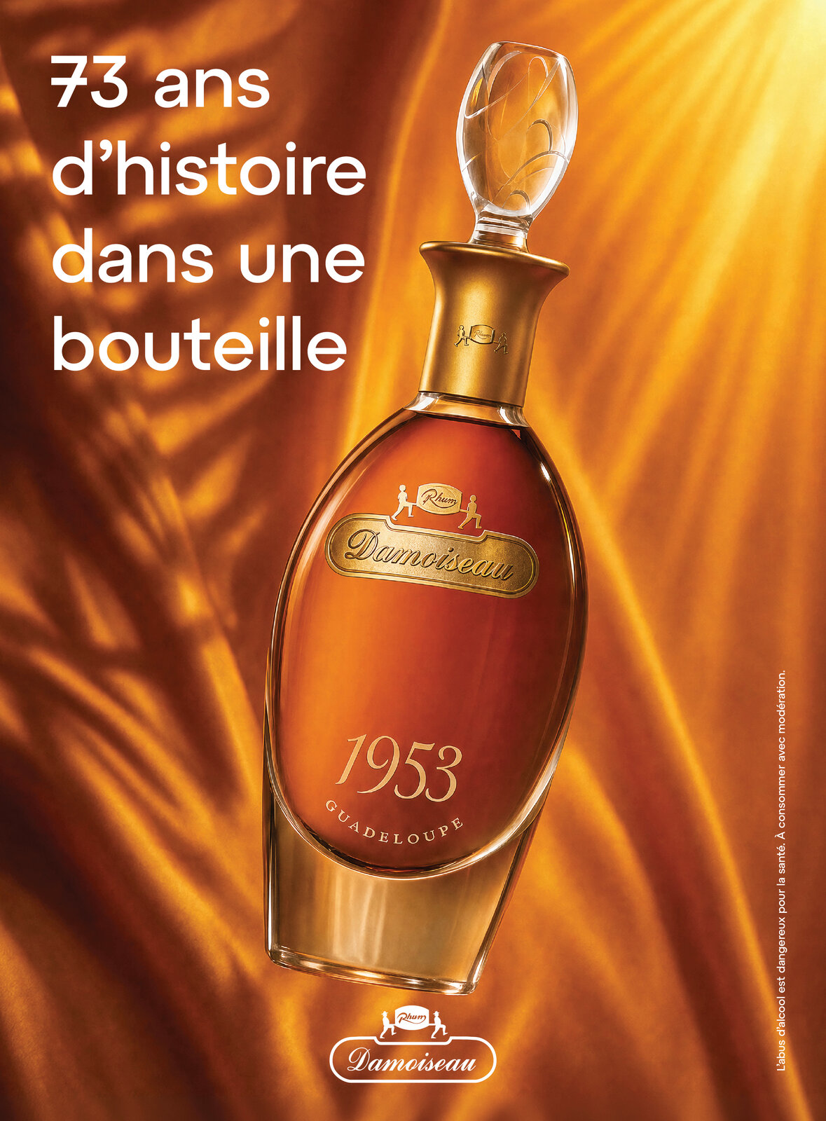 Damoiseau 1953 : l’annonce presse « 73 ans d’histoire dans une bouteille », la carafe de rhum ambré et son bouchon de verre, sur un drapé doré strié d’ombres de palmes