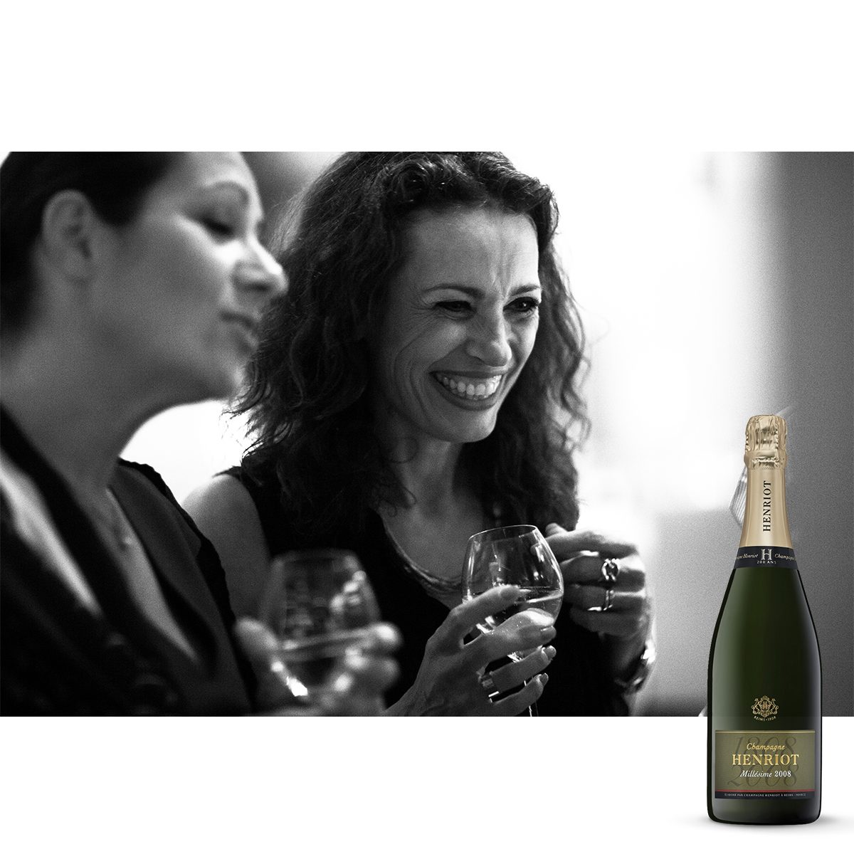Champagne Henriot : deux femmes rient, un verre à la main, en noir et blanc, et la bouteille