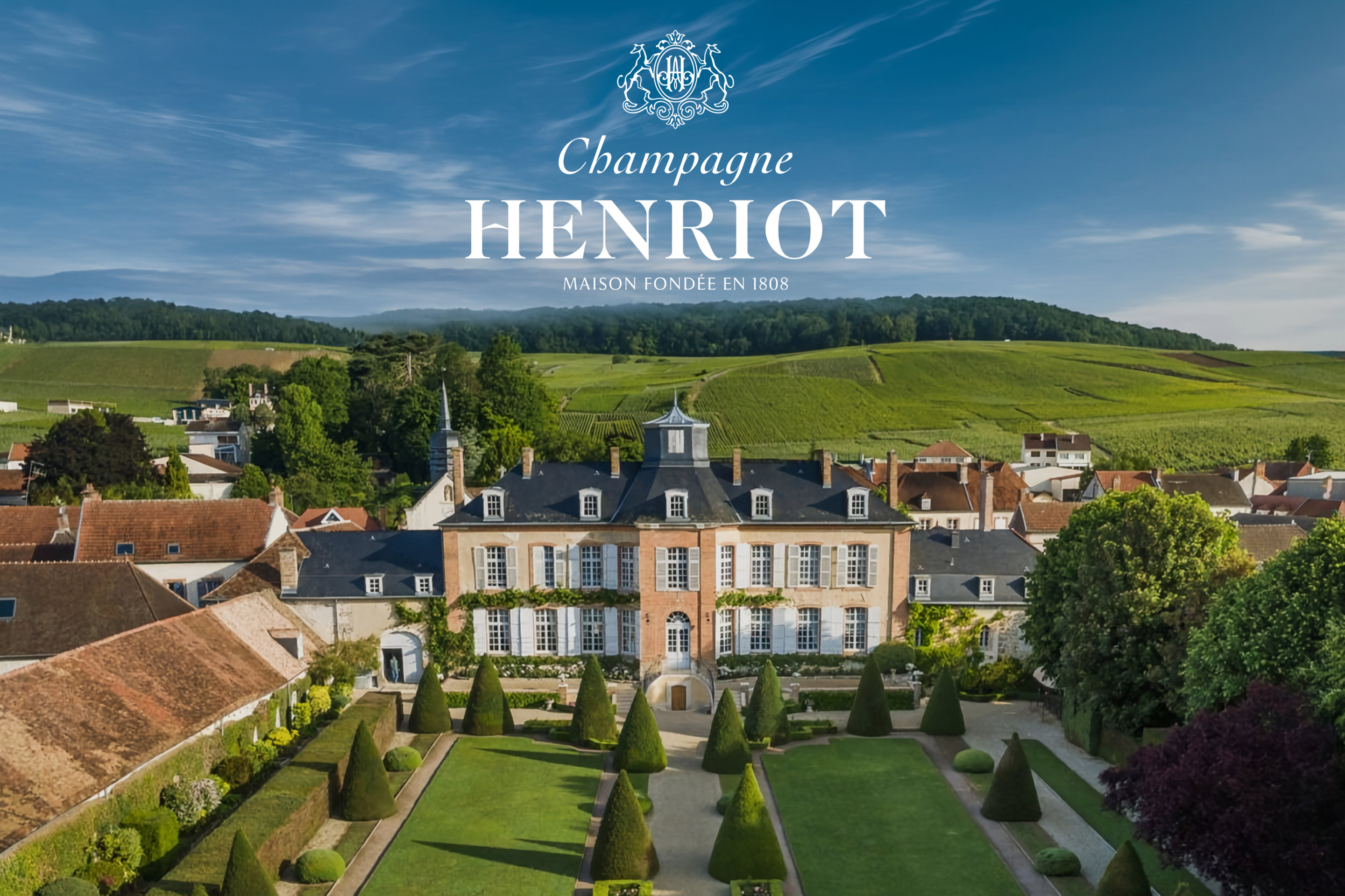 Champagne Henriot : le logo de la Maison fondée en 1808 au-dessus du domaine, sa demeure et ses jardins, les vignes sur les coteaux